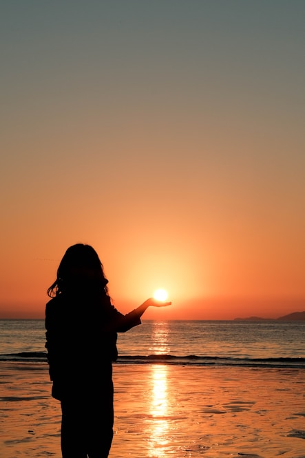 Silhouette of a person holding the sun at sunset.
