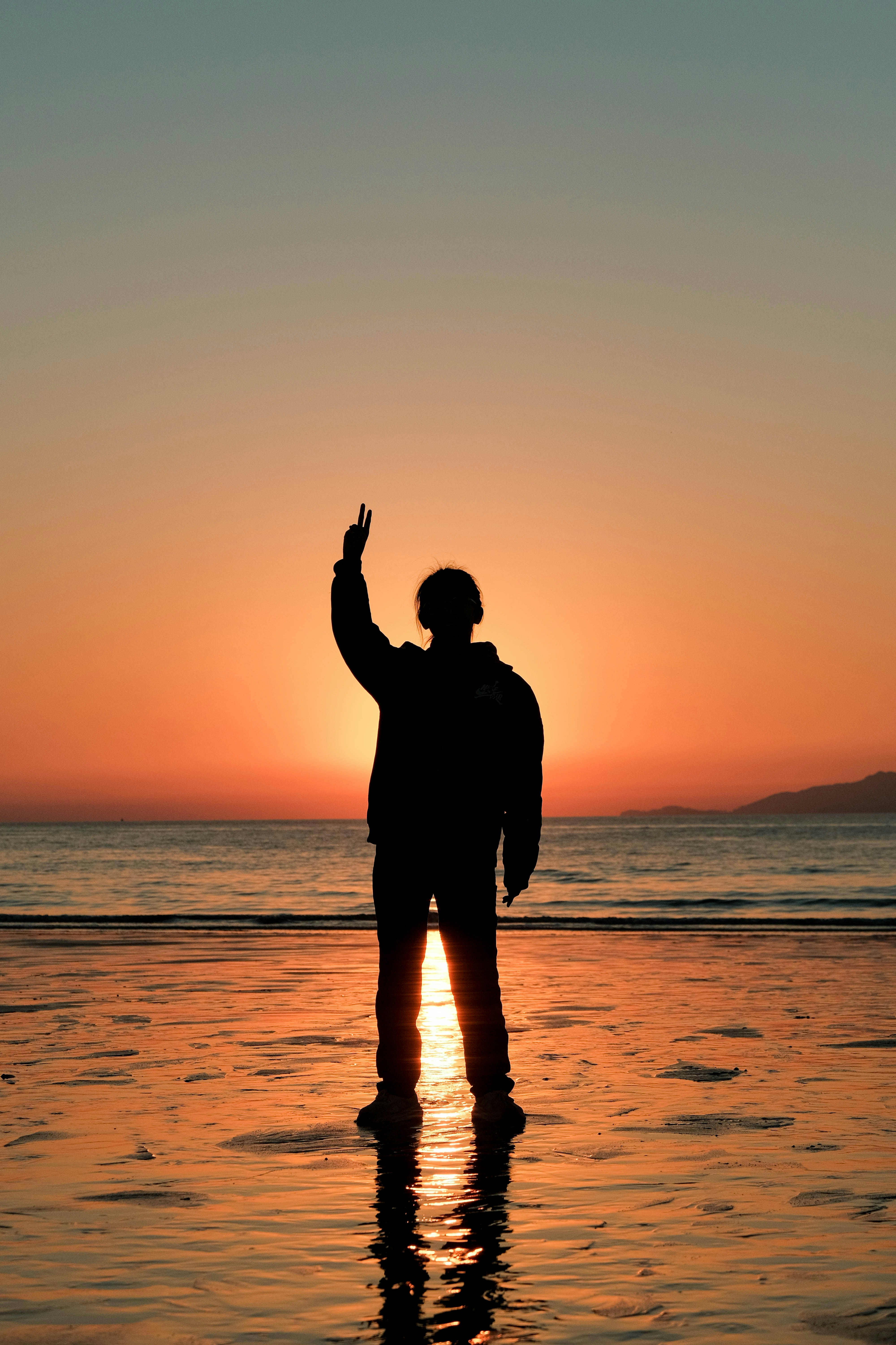 Silhouette of a person waving at sunset on the beach.