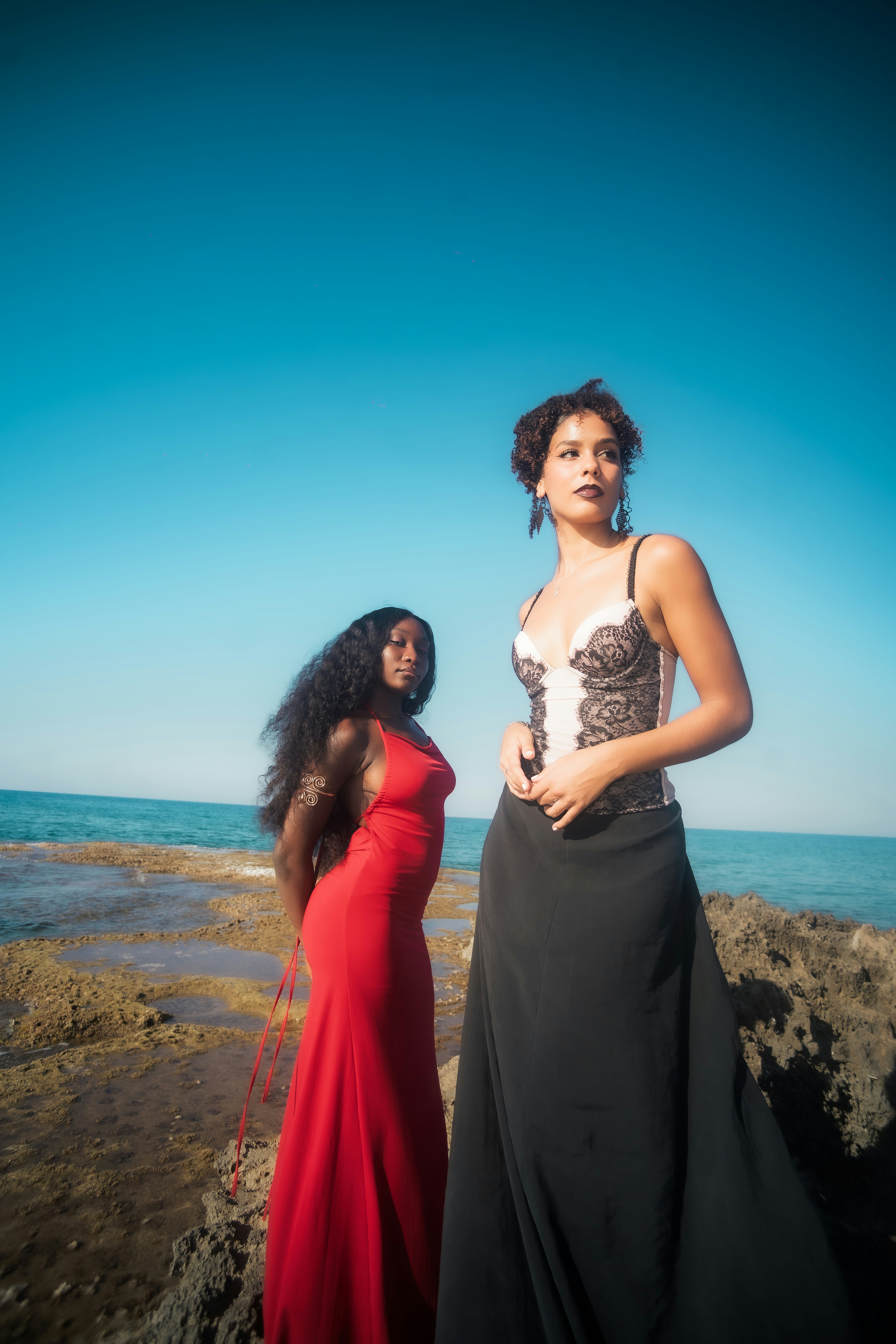 Two women in formal dresses on a rocky shore.