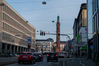 Cars driving on a city street with buildings and tower.