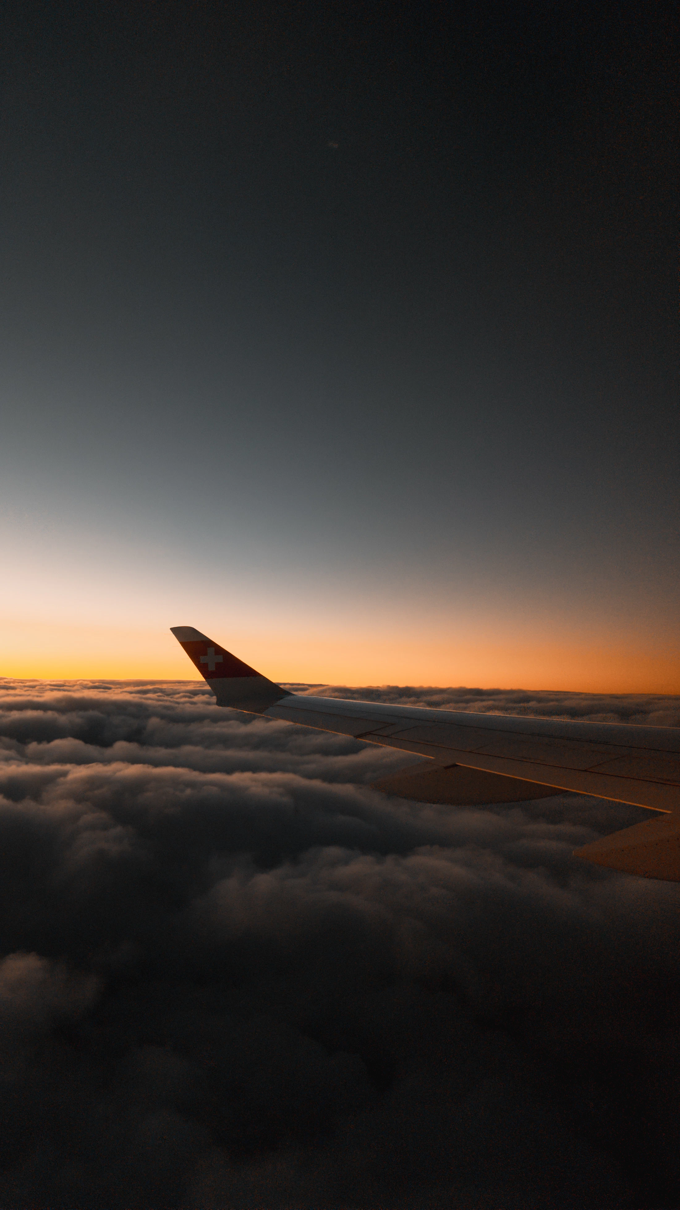 Airplane wing above the clouds at sunset