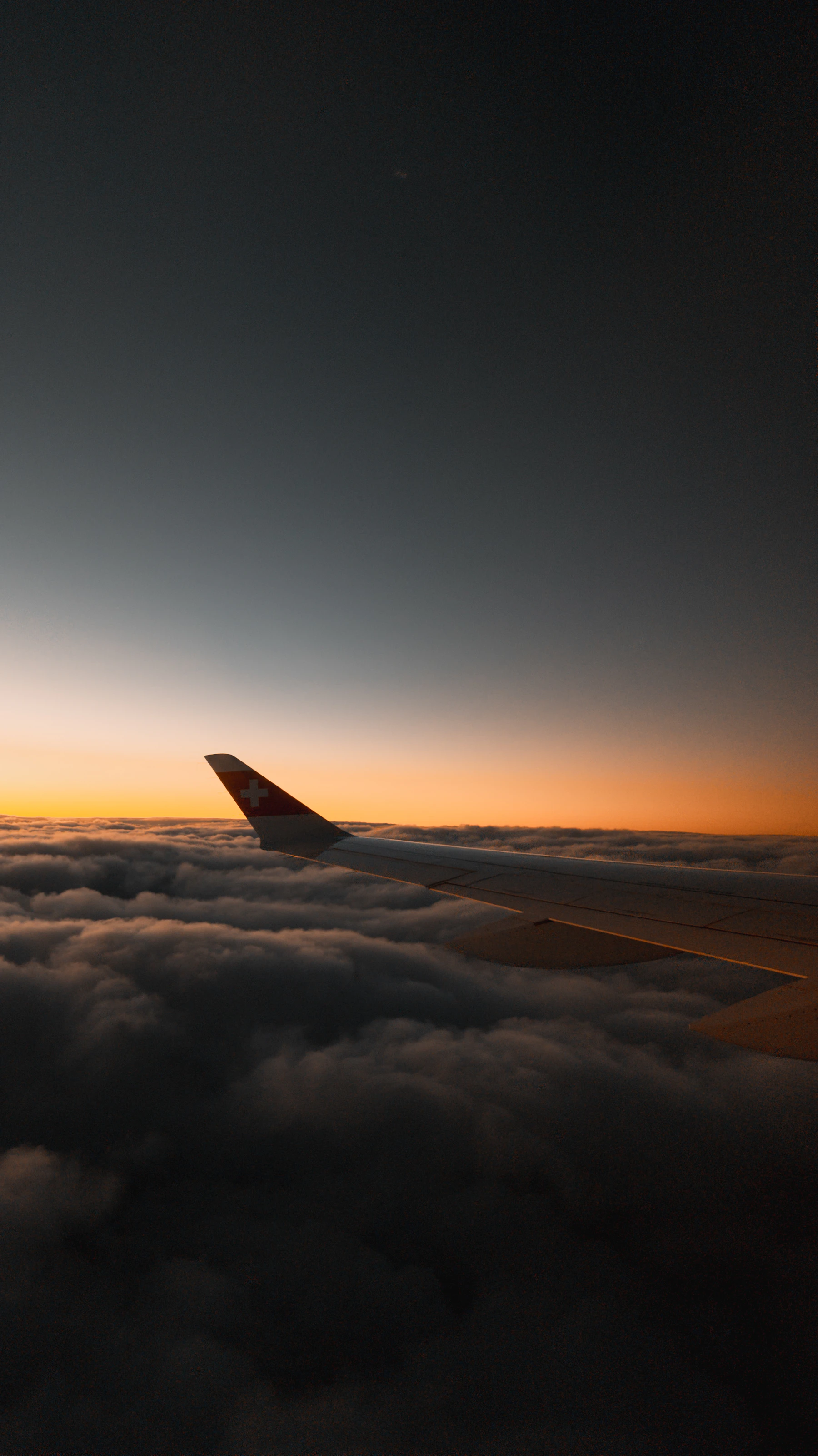 Airplane wing above the clouds at sunset