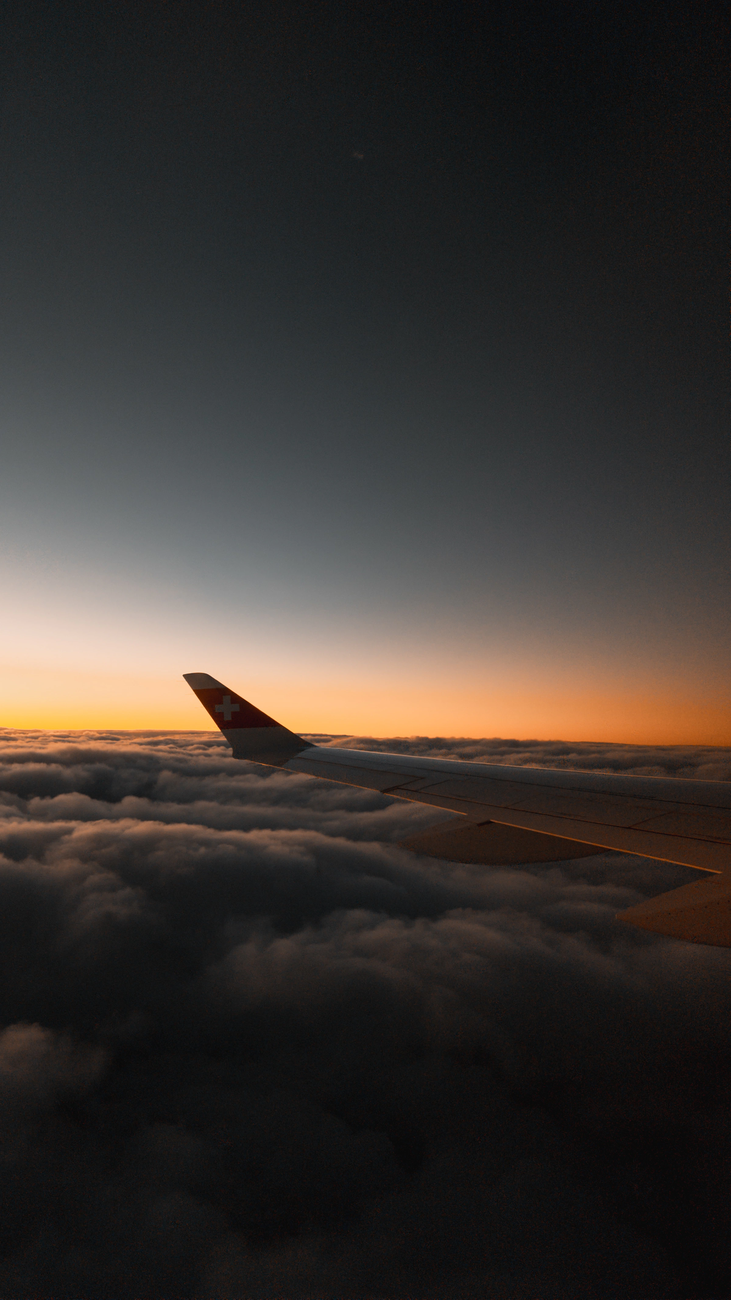 Airplane wing gliding above illuminated clouds at sunset