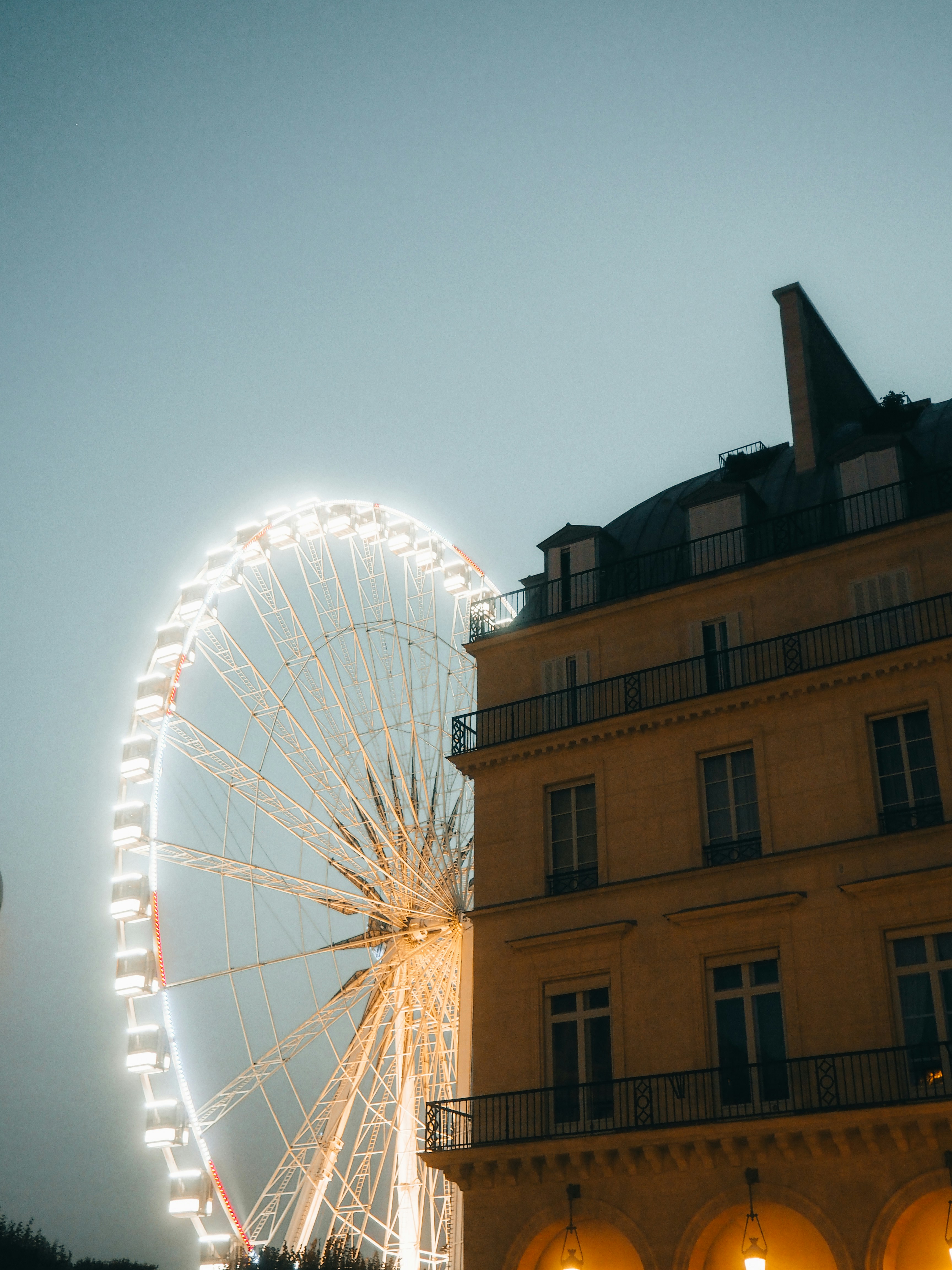 Illuminated ferris wheel next to a building at dusk
