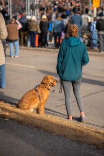 Woman and dog wait by a street with crowd