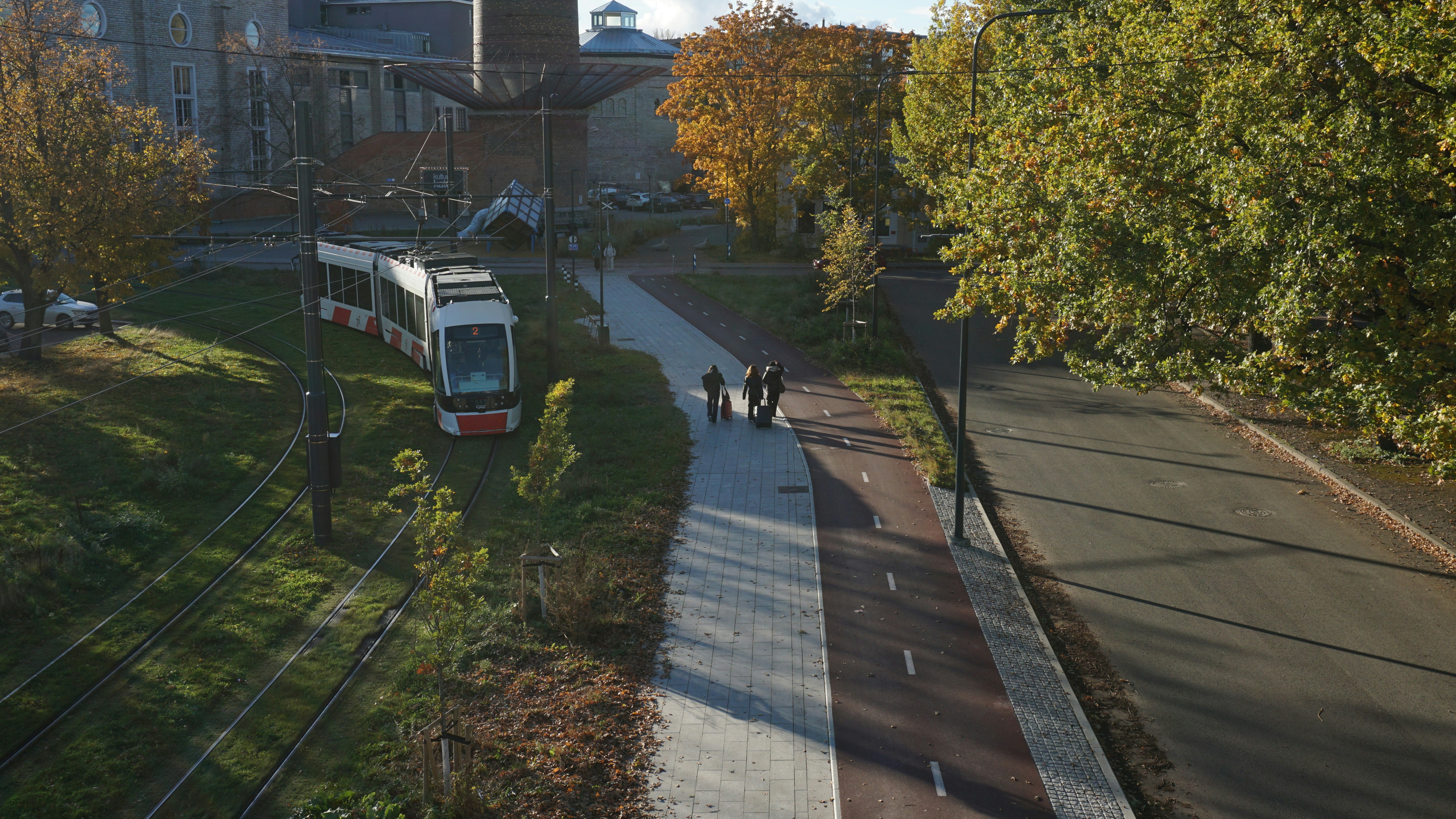 Tram on tracks near a park with trees