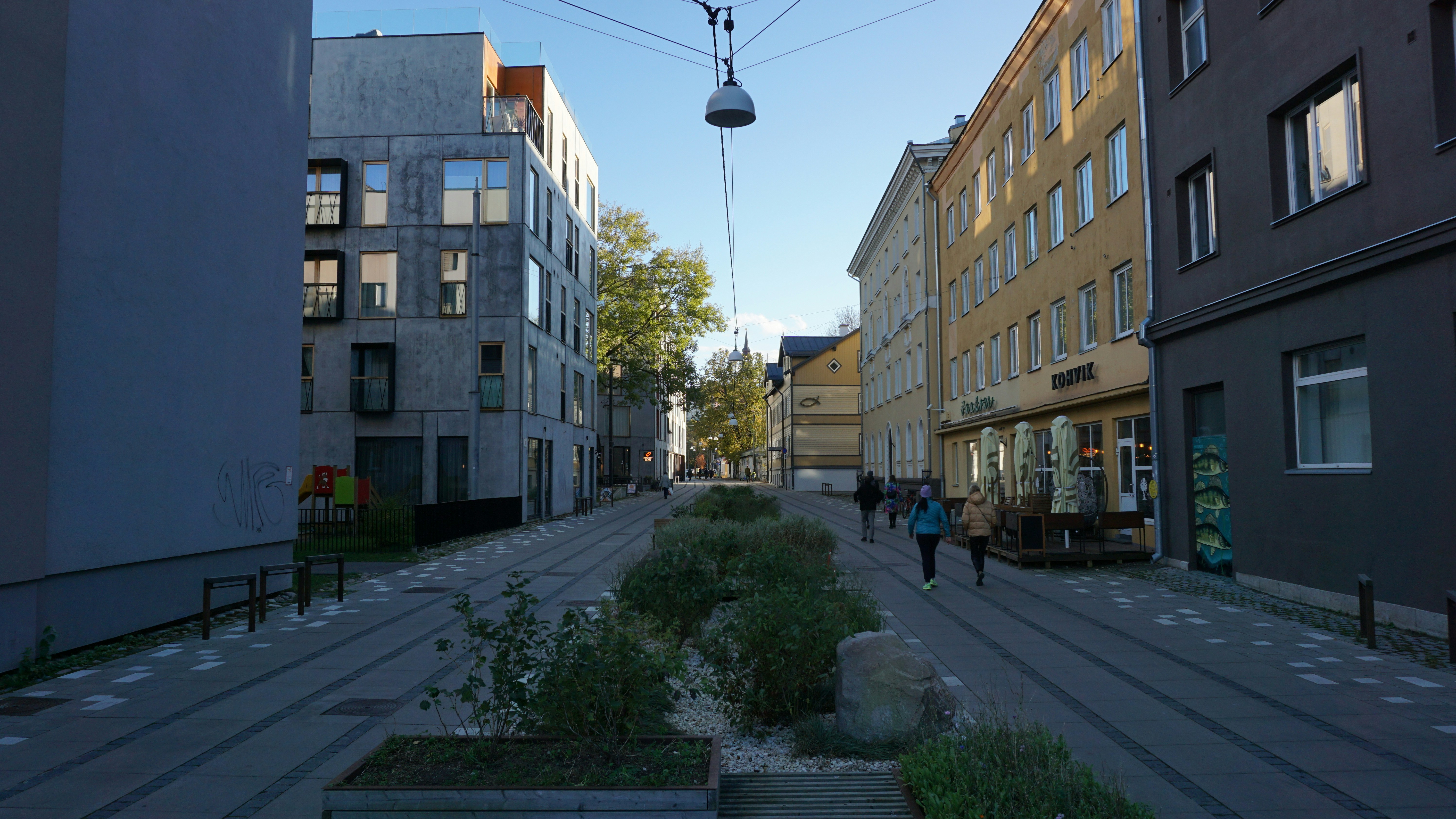 People walk down a modern city street with planters.