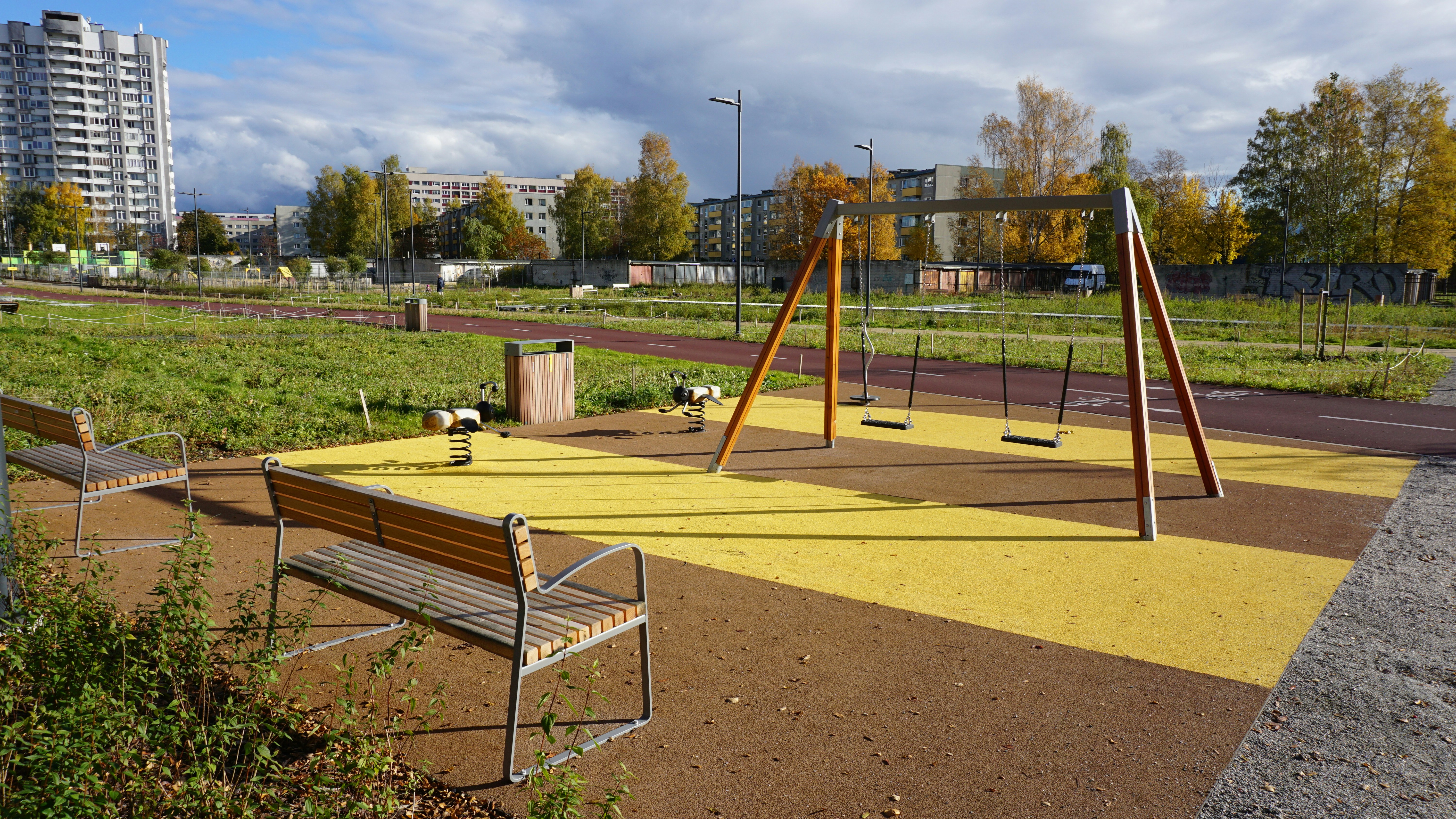 Empty playground with swings and benches on a sunny day.