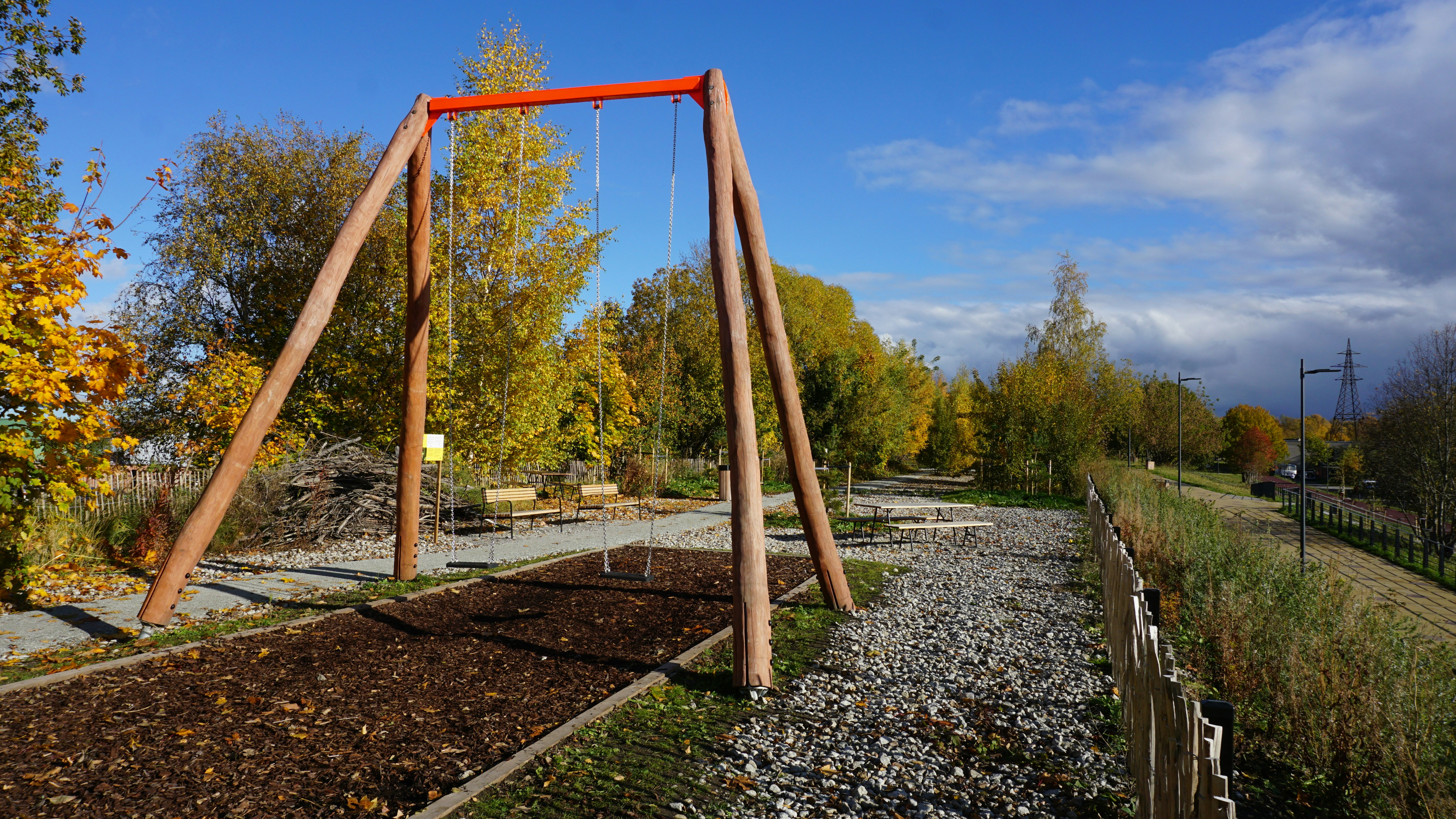Wooden swing set in a park with autumn foliage.
