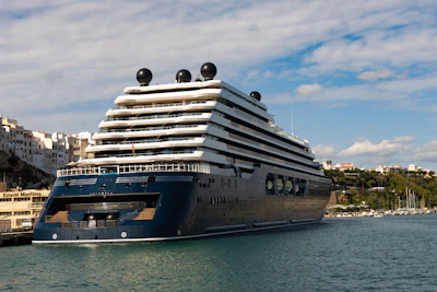 A large dark blue cruise ship docked in a harbor.