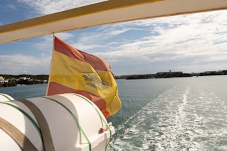 Spanish flag waving on a boat with coastline ahead
