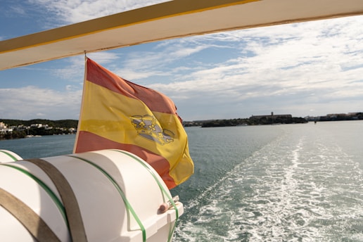 Spanish flag waving on a boat with coastline ahead