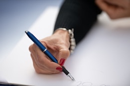 A hand writing with a blue pen on paper.
