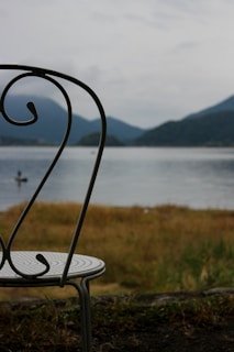Empty chair overlooking a calm lake and mountains.