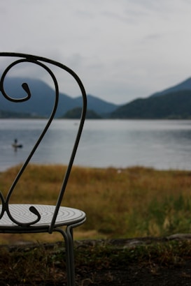 Empty chair overlooking a calm lake and mountains.