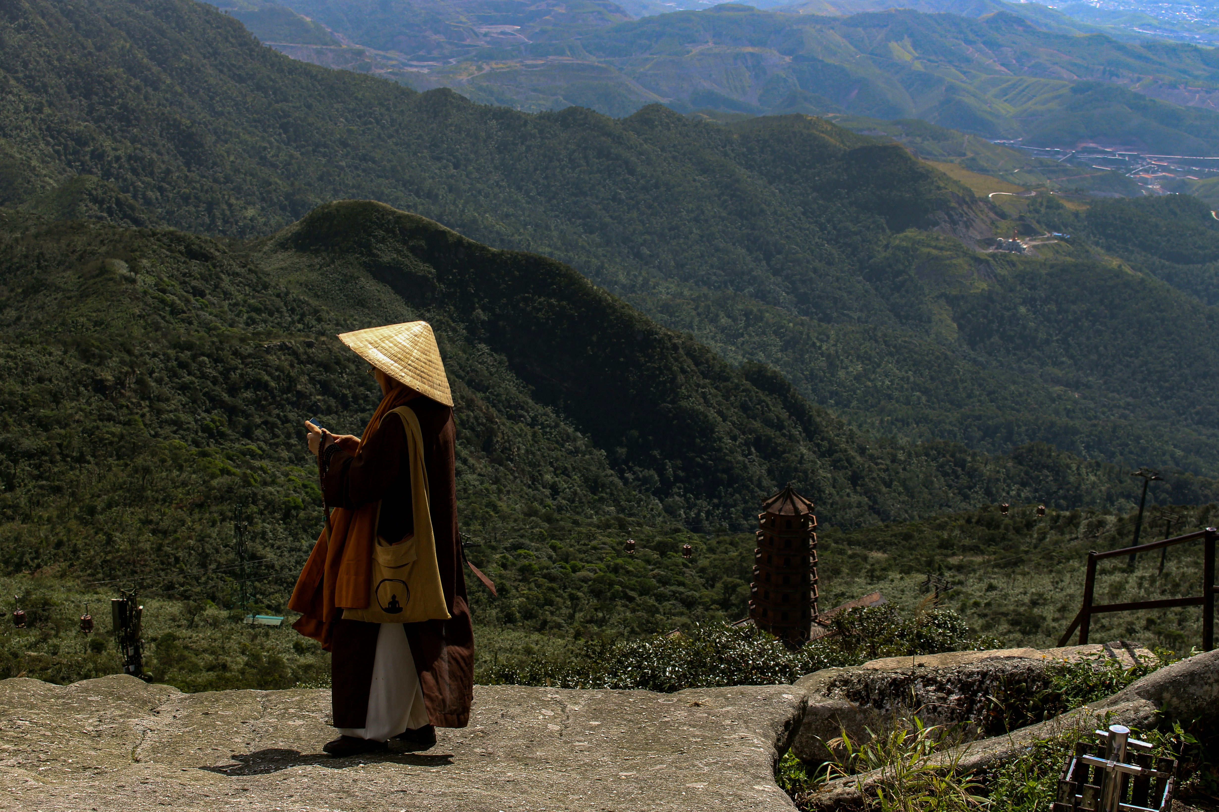 Monje con sombrero tradicional contempla montañas verdes y exuberantes.