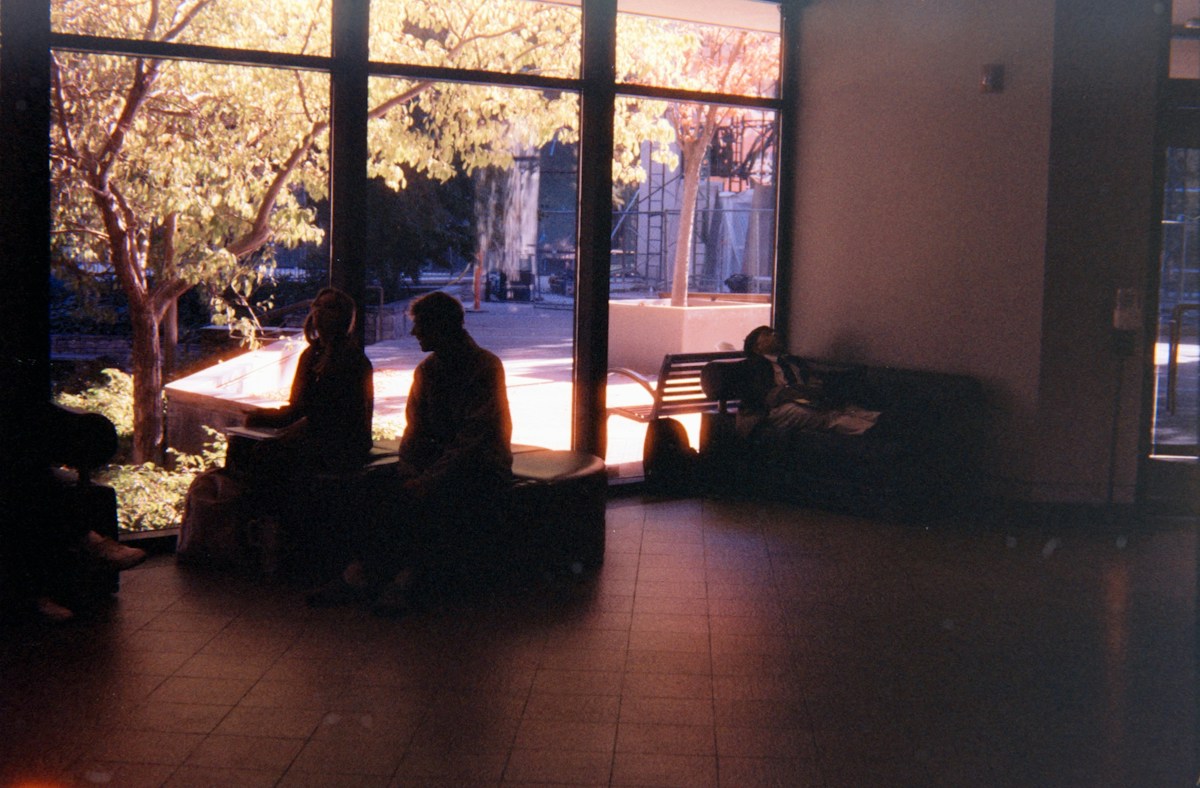 Silhouettes of college students sitting by a large window, possibly enjoying healthy dorm snacks while studying.