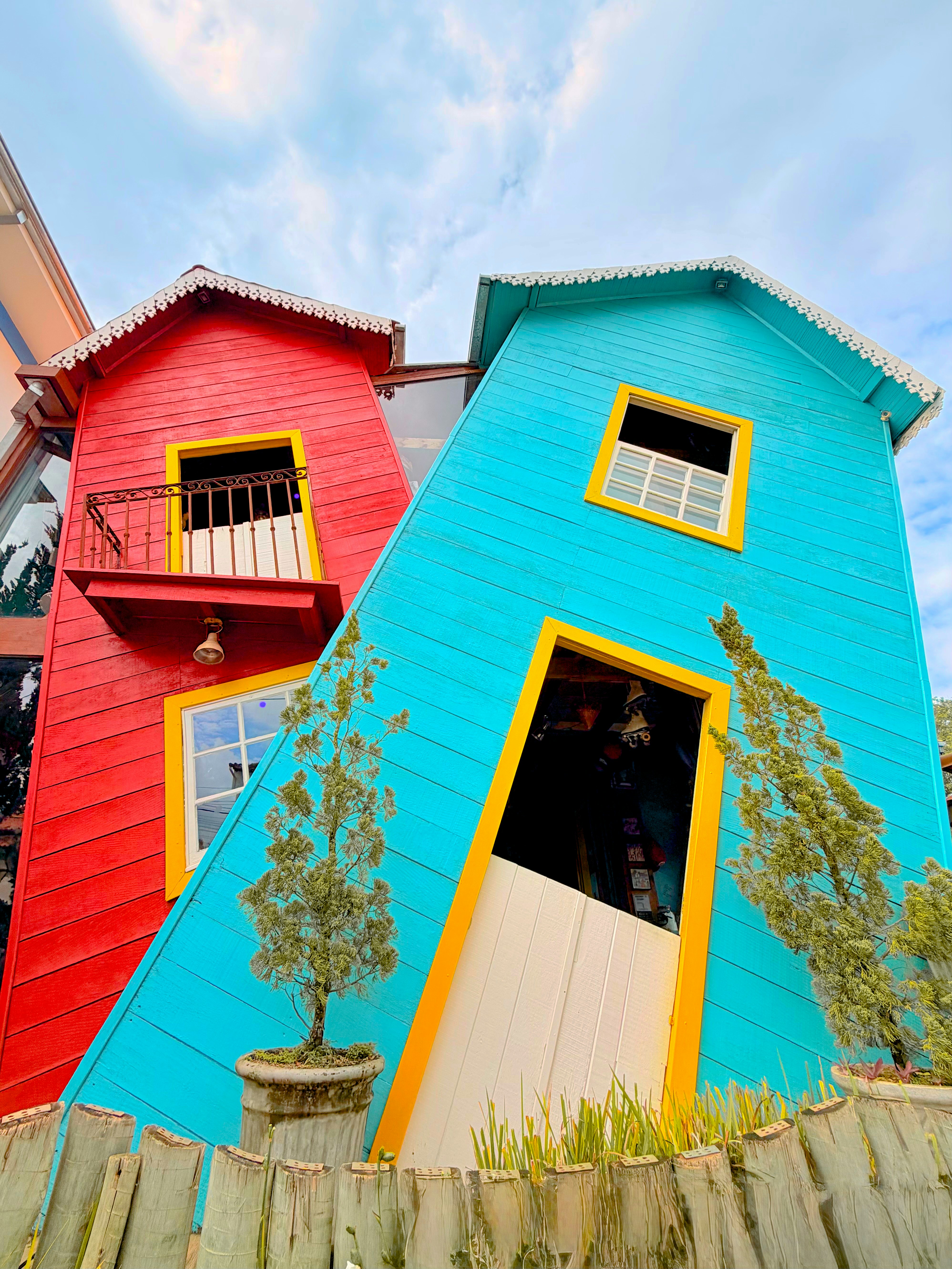 Two colorful, tilted houses against a cloudy sky.