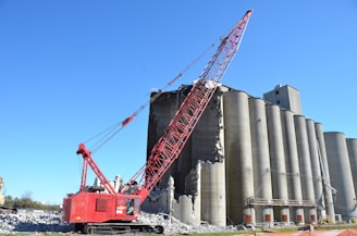 Crane demolishing concrete silos against clear blue sky.