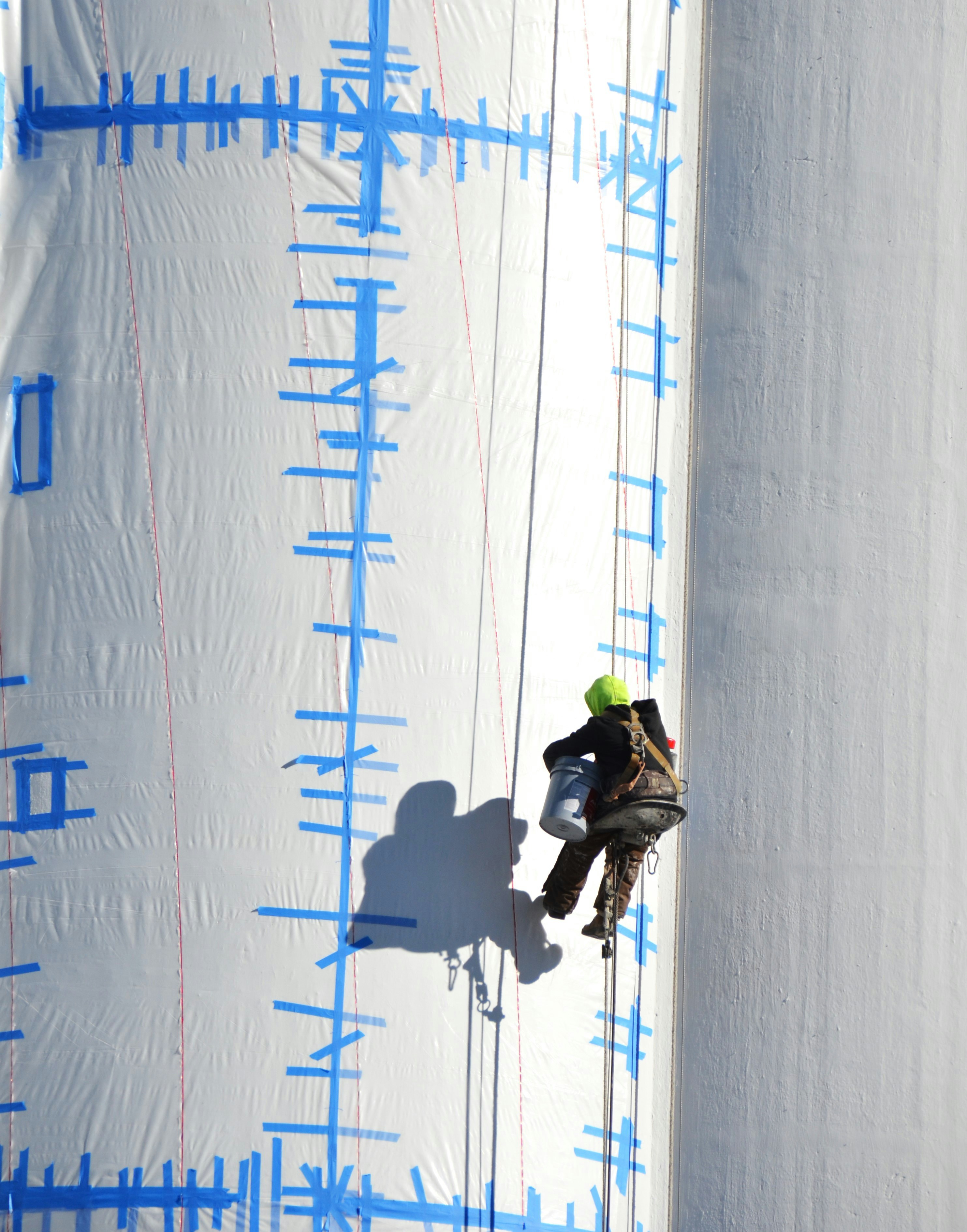 O trabalhador desce em rapel por uma grande estrutura branca.