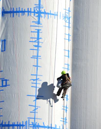 Worker rappels down a large white structure.