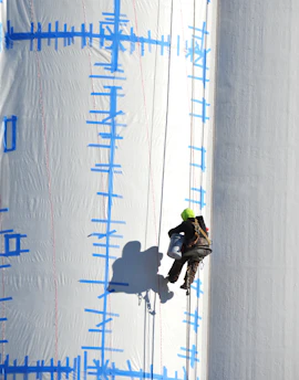 Worker rappels down a large white structure.