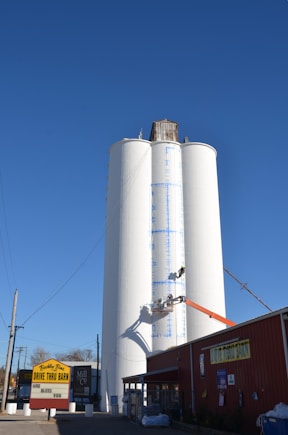Workers paint a tall white silo against blue sky.