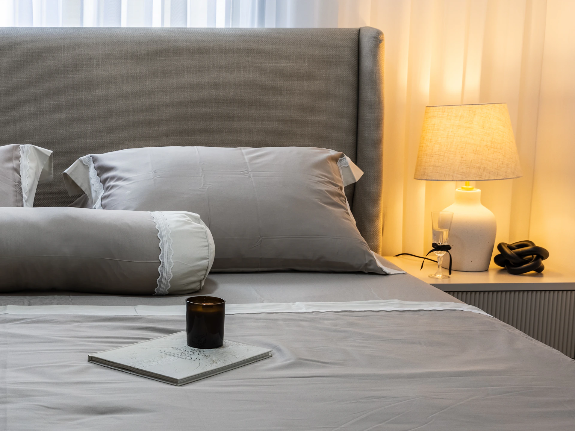 Lit élégant avec linge gris dans une chambre à la lumière chaude