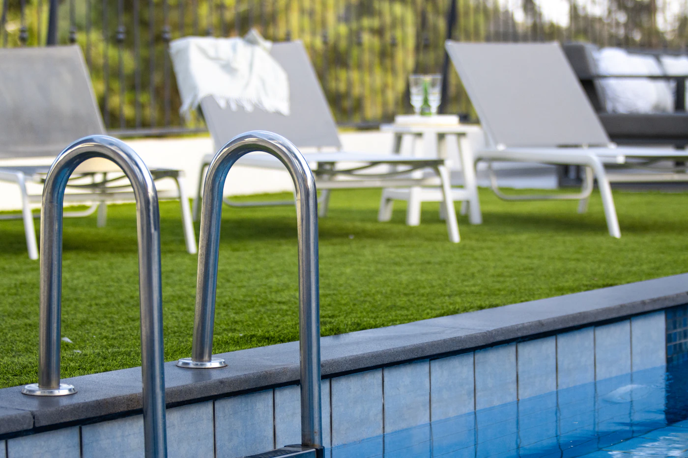 Swimming pool ladder beside lounge chairs on a lawn ready for the season