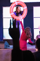 Woman holds life preserver for child on stage.