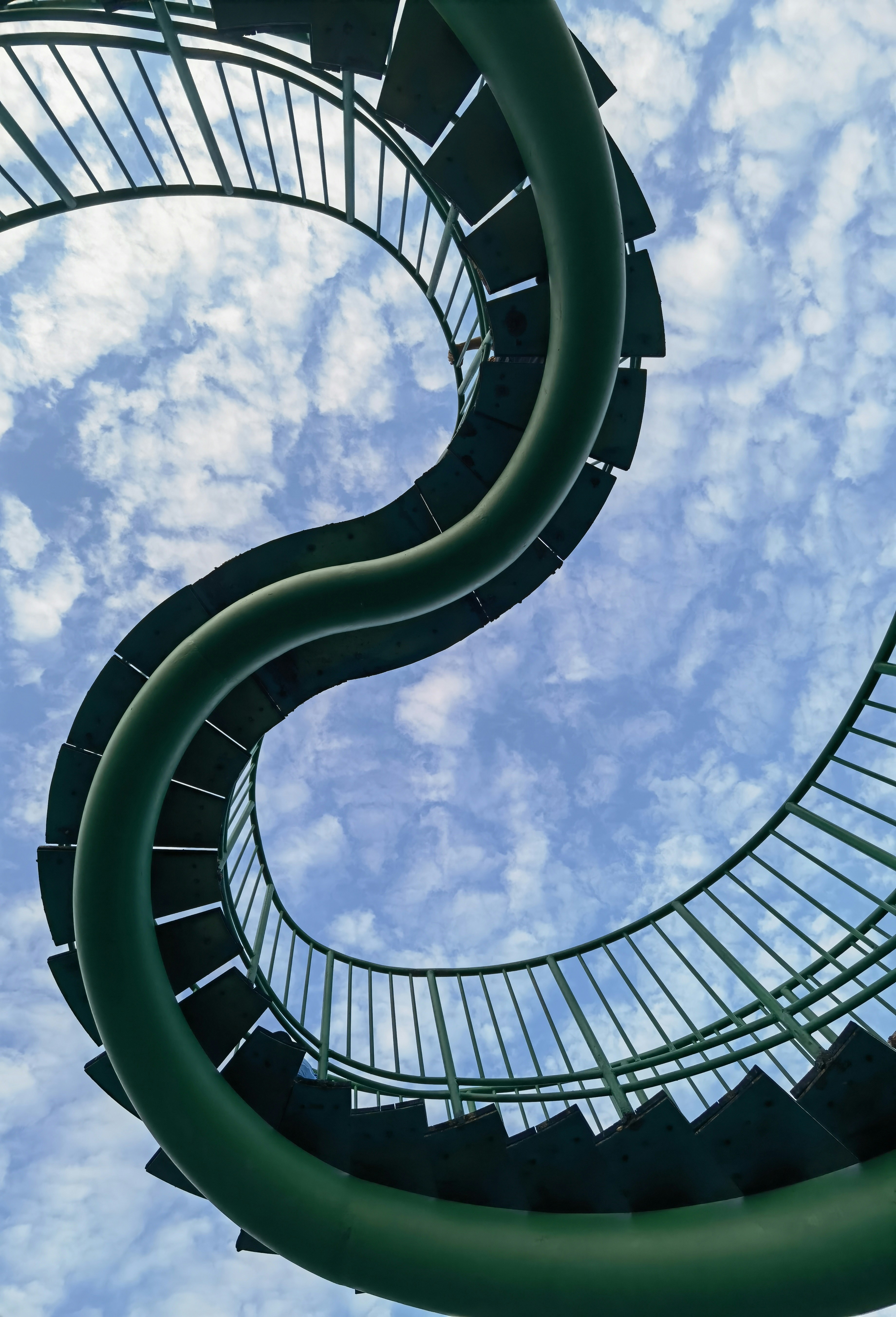 Curving green staircase against a cloudy blue sky
