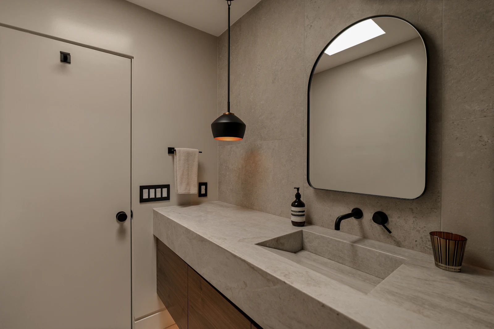 Bathroom with a long concrete basin, wall-mounted black tap, arched mirror and a single pendant