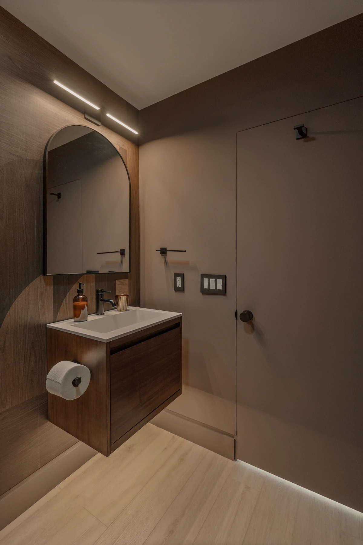Custom bathroom vanity cabinetry with wood front, floating drawers, arched mirror, and integrated lighting