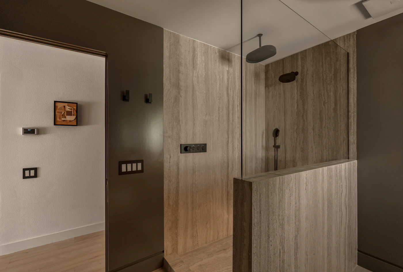 Walk-in shower with travertine walls and a half-height glass panel