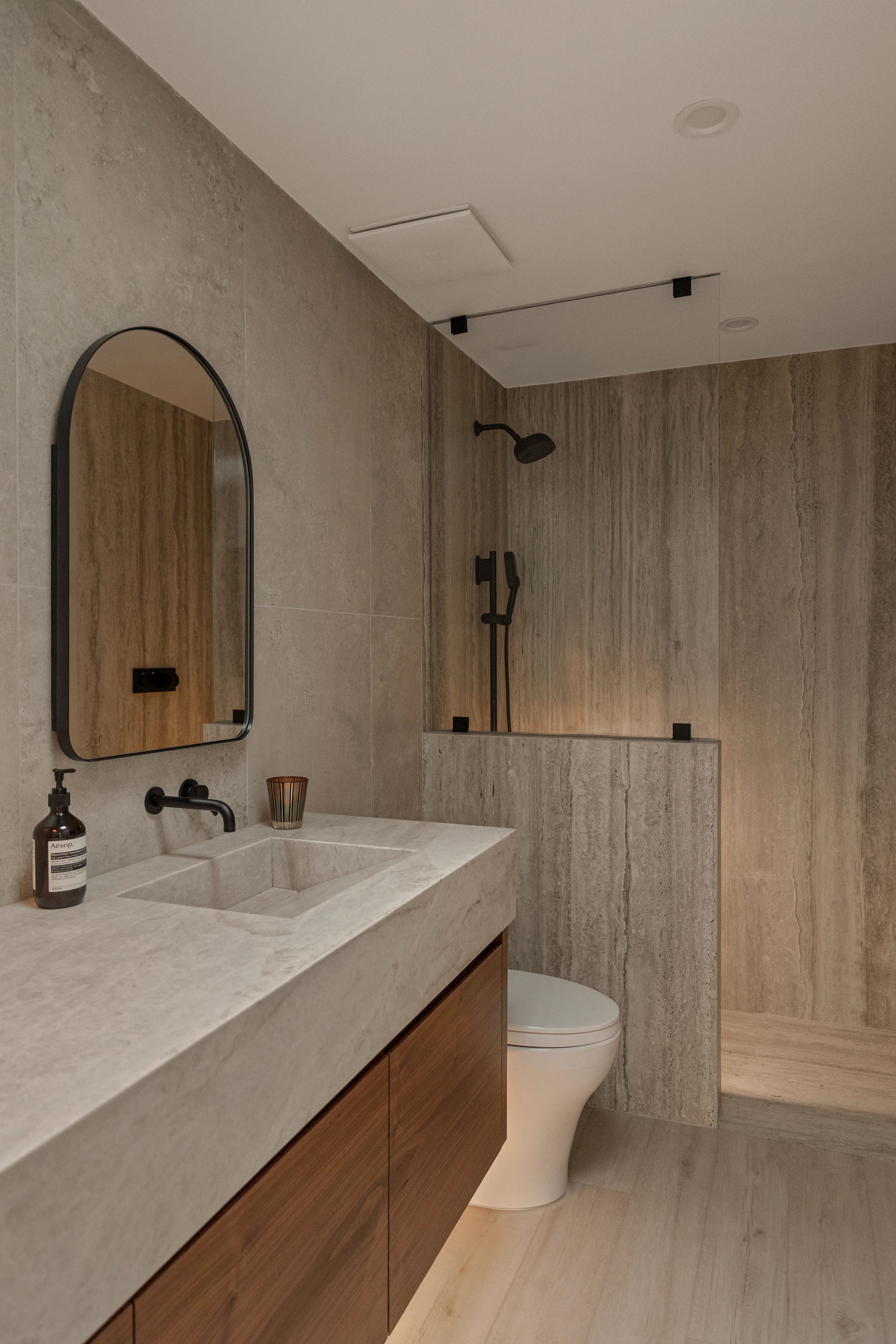 Modern bathroom with stone tiles and wooden vanity.