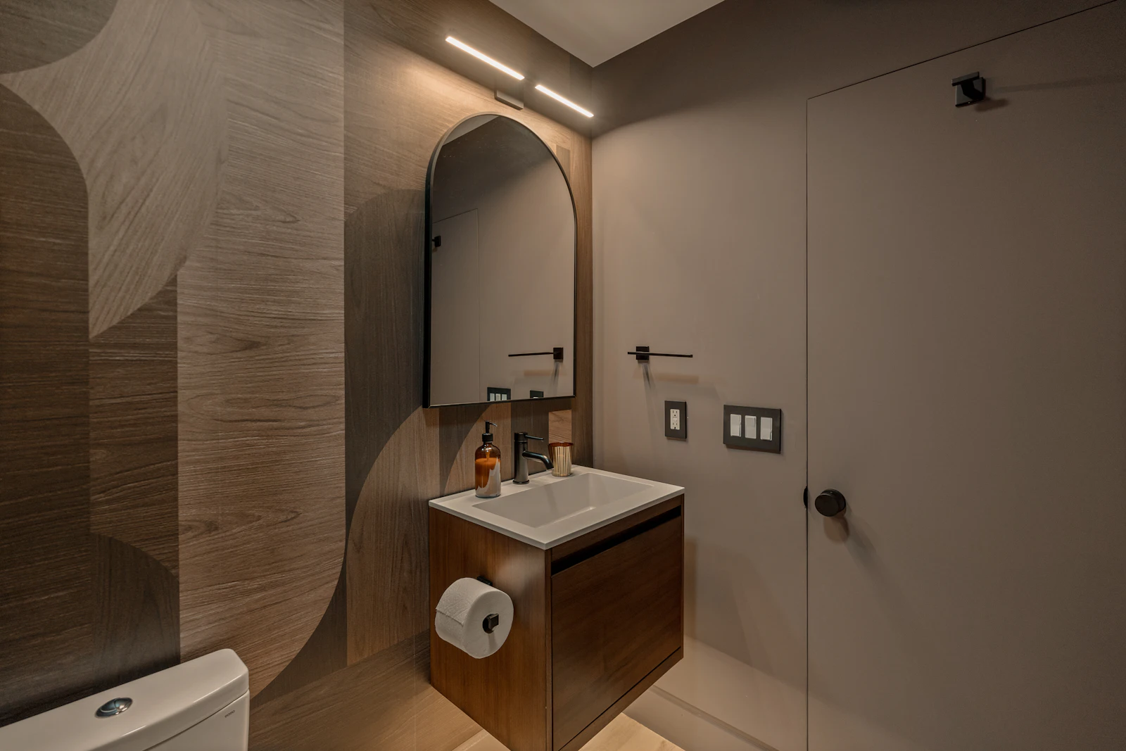 Baño con vanitory de madera, espejo arqueado y lámpara colgante negra