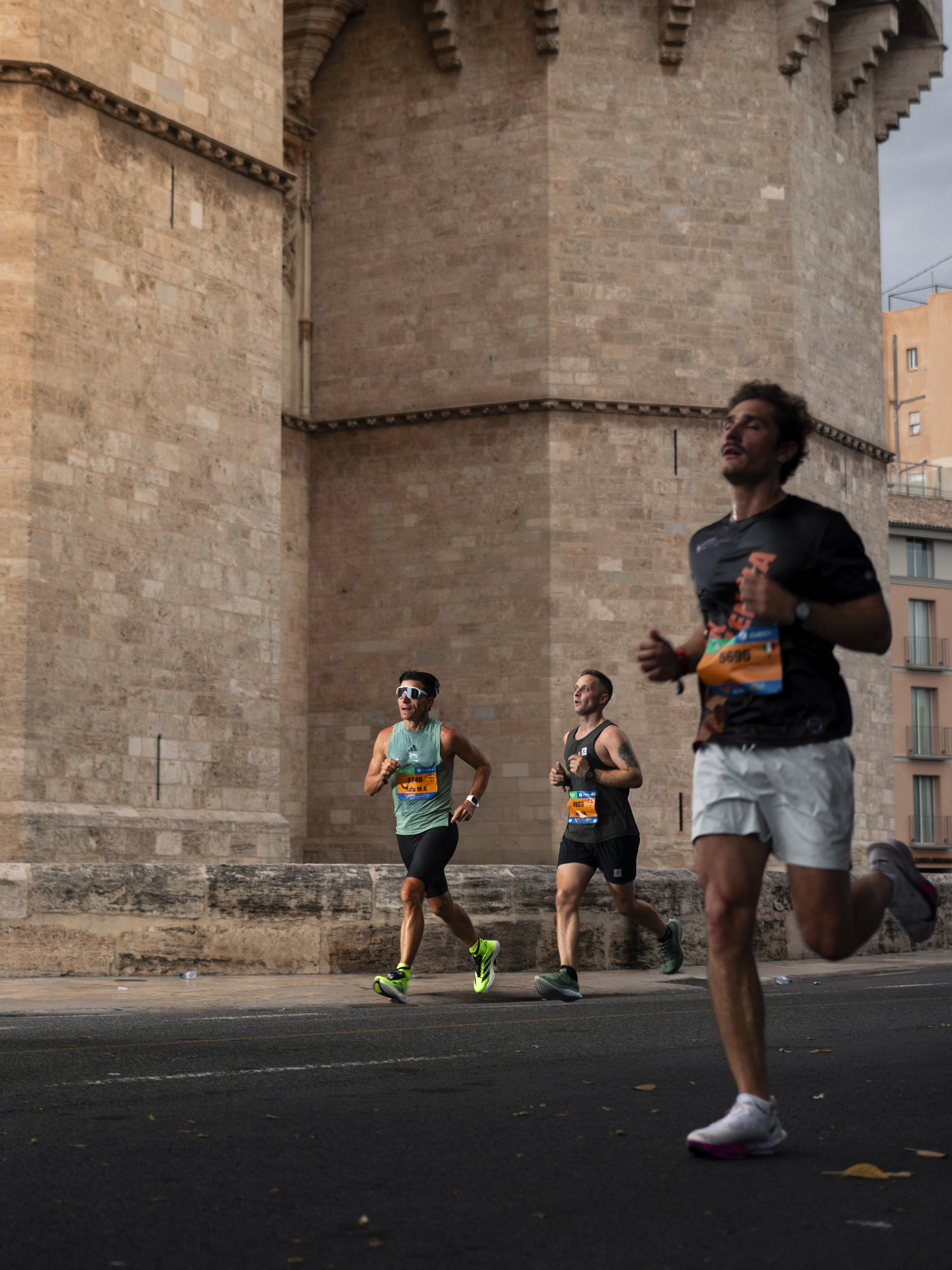 Marathon runners pass beneath the round towers of a medieval stone gate in Valencia.