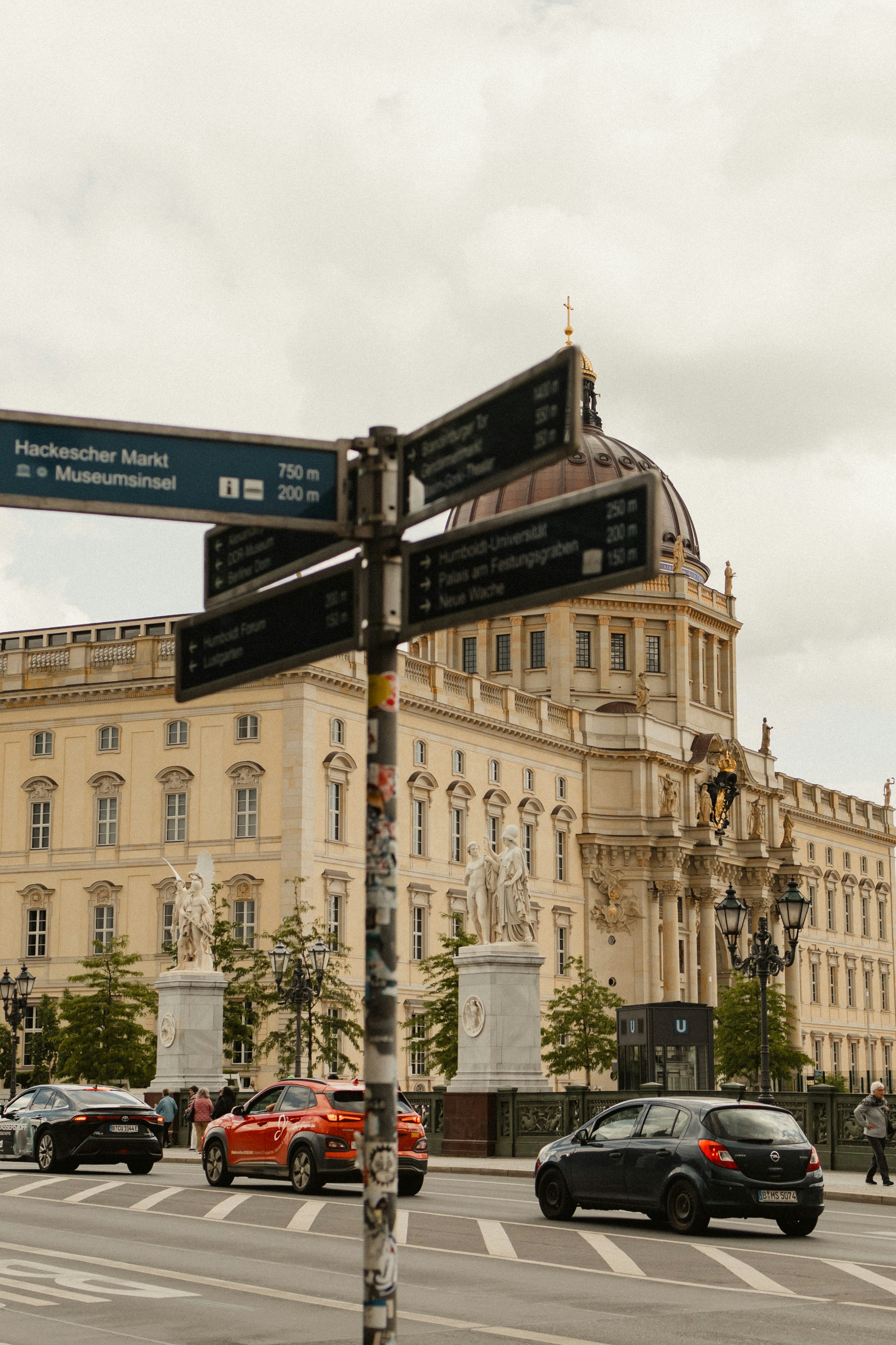 Street signs point towards landmarks near a grand building.