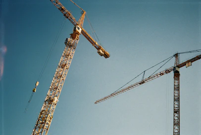 Two construction cranes against a clear blue sky
