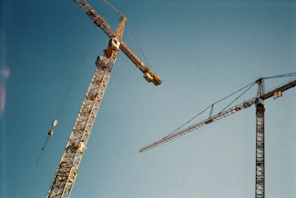 Two construction cranes against a clear blue sky