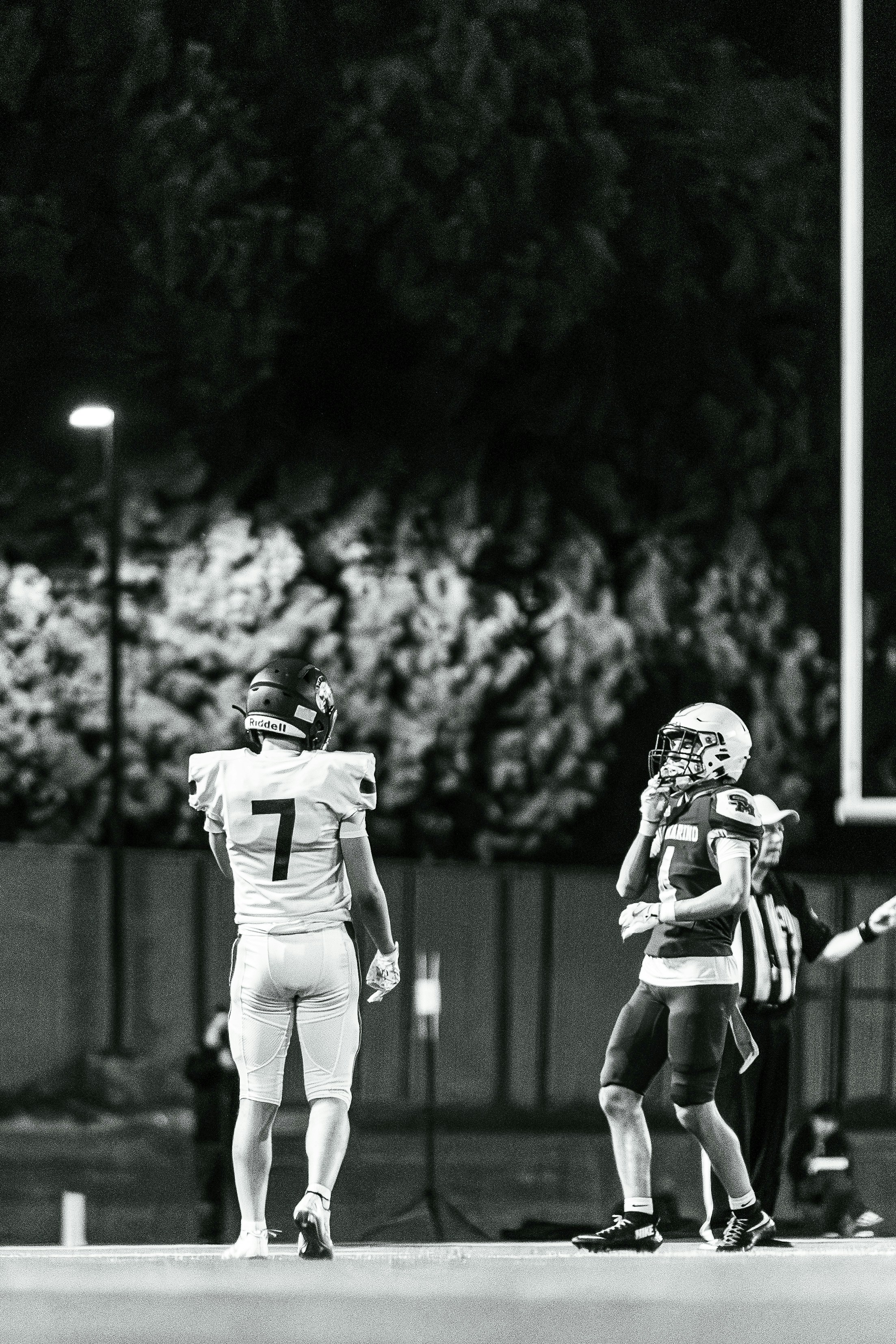 Two football players on the field at night.