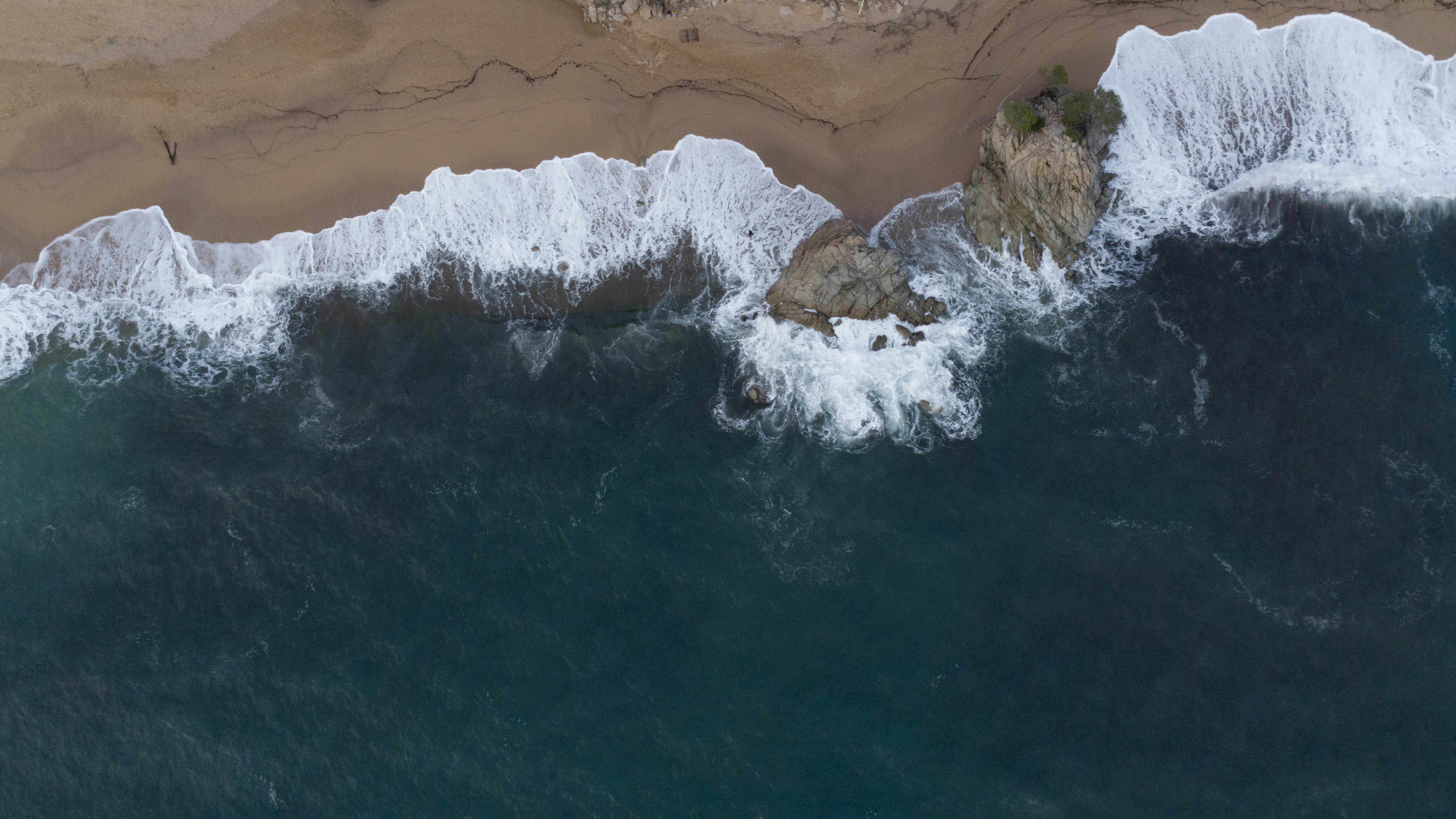 Waves crash on a rocky shore from above.