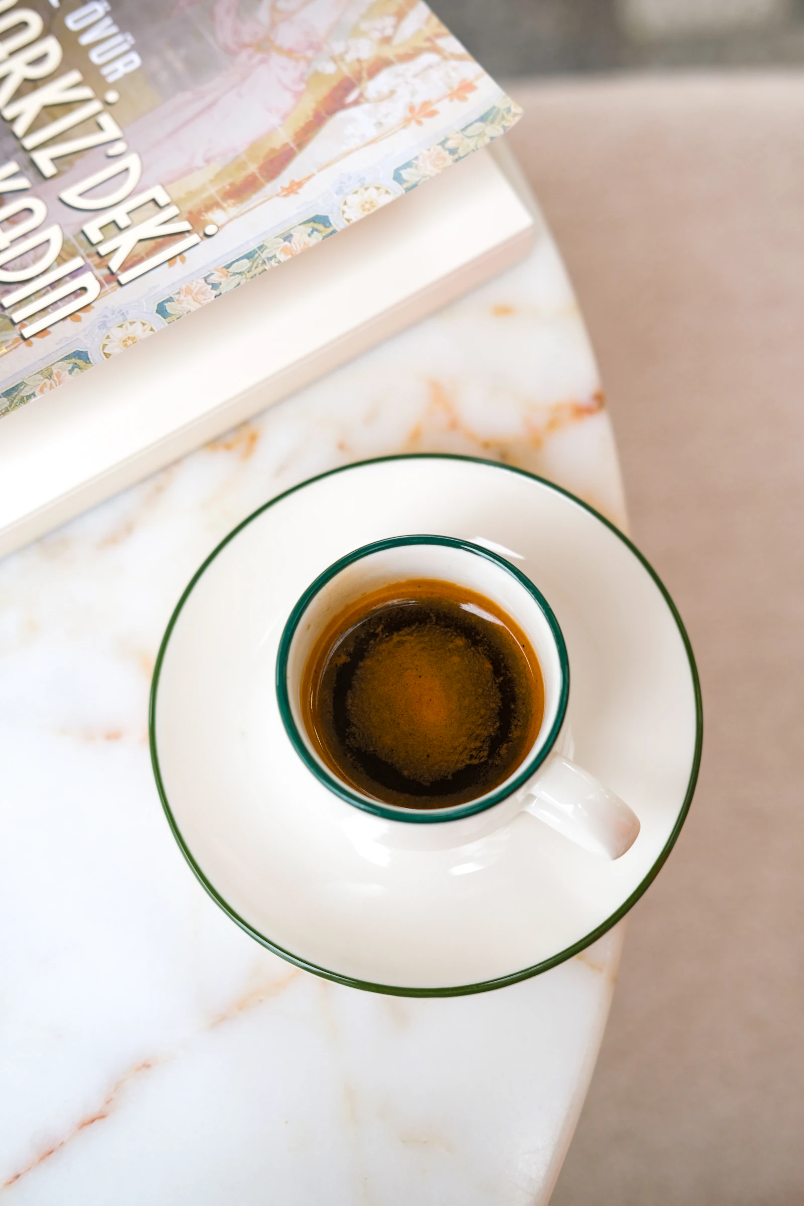 A cup of coffee beside a neat stack of books on a warm rustic surface