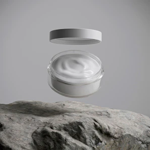 A jar of white cream floats above a rock.