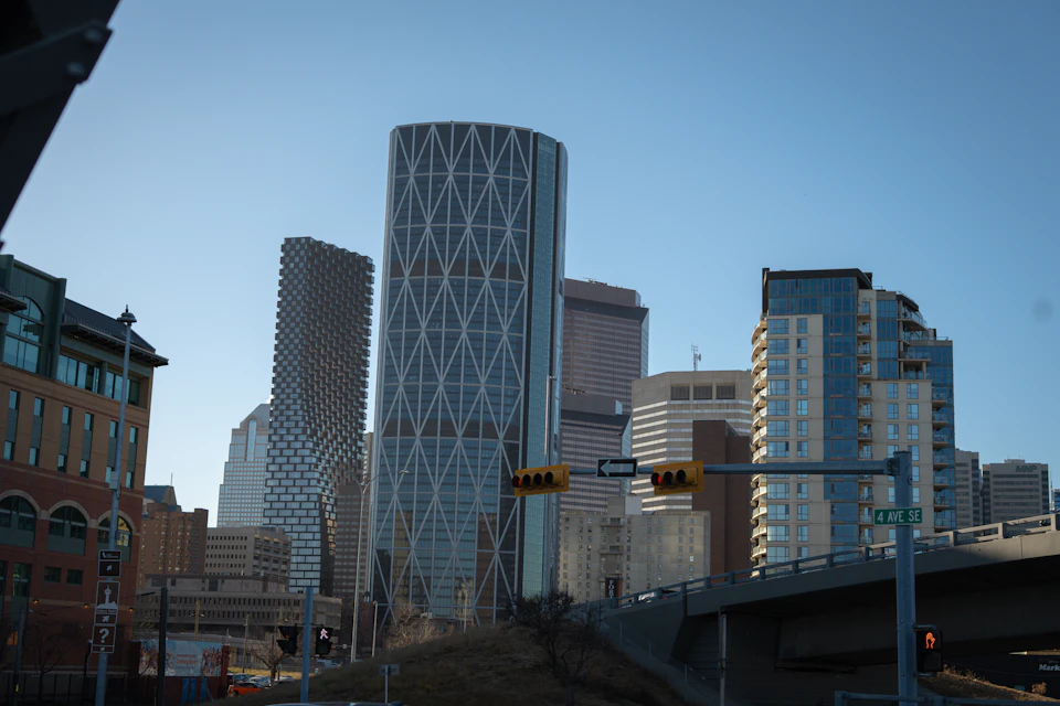 Tall modern skyscraper dominates cityscape with grid-like patterned cylinder in background