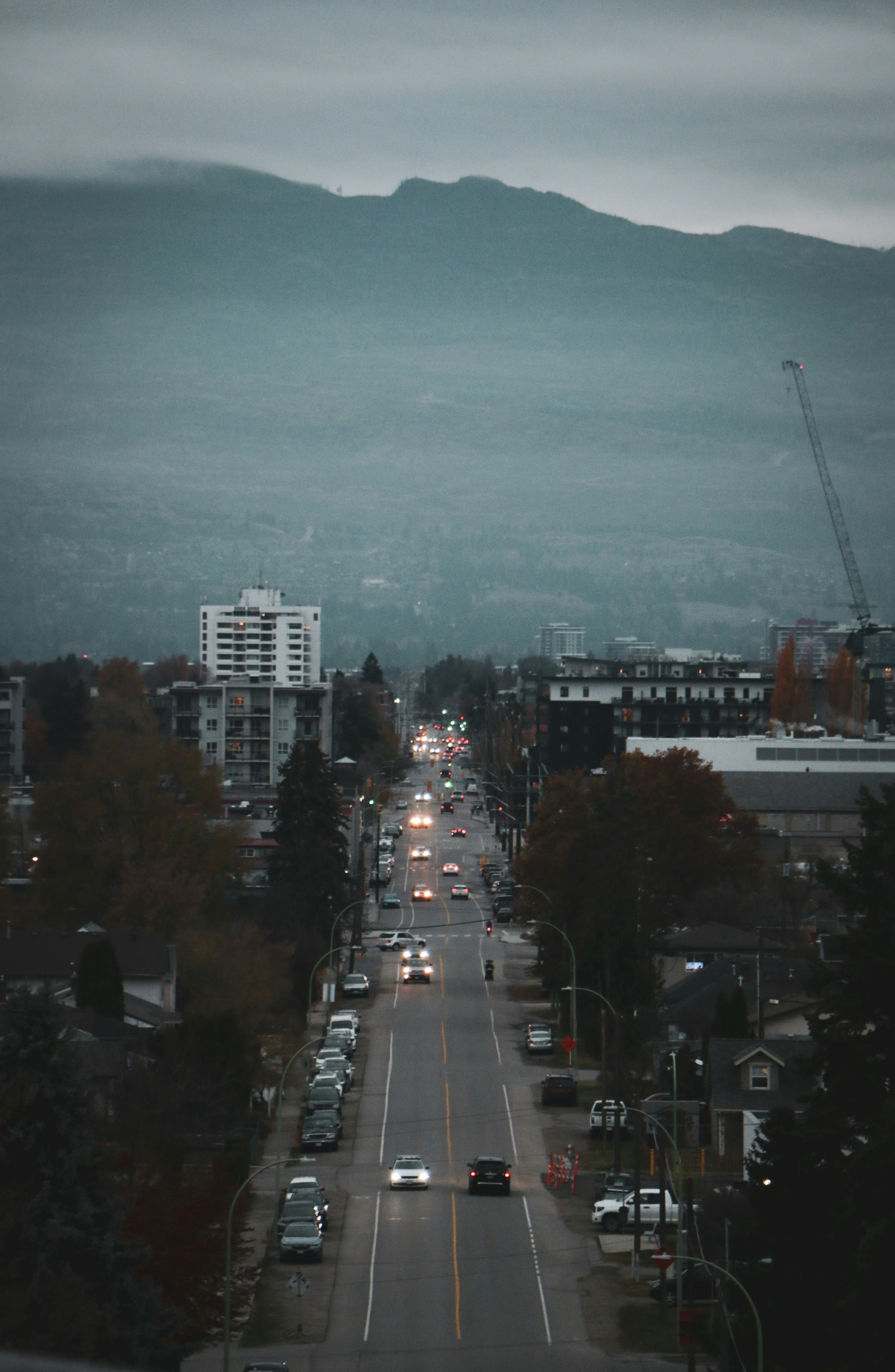 Cars driving down a city street towards mountains.