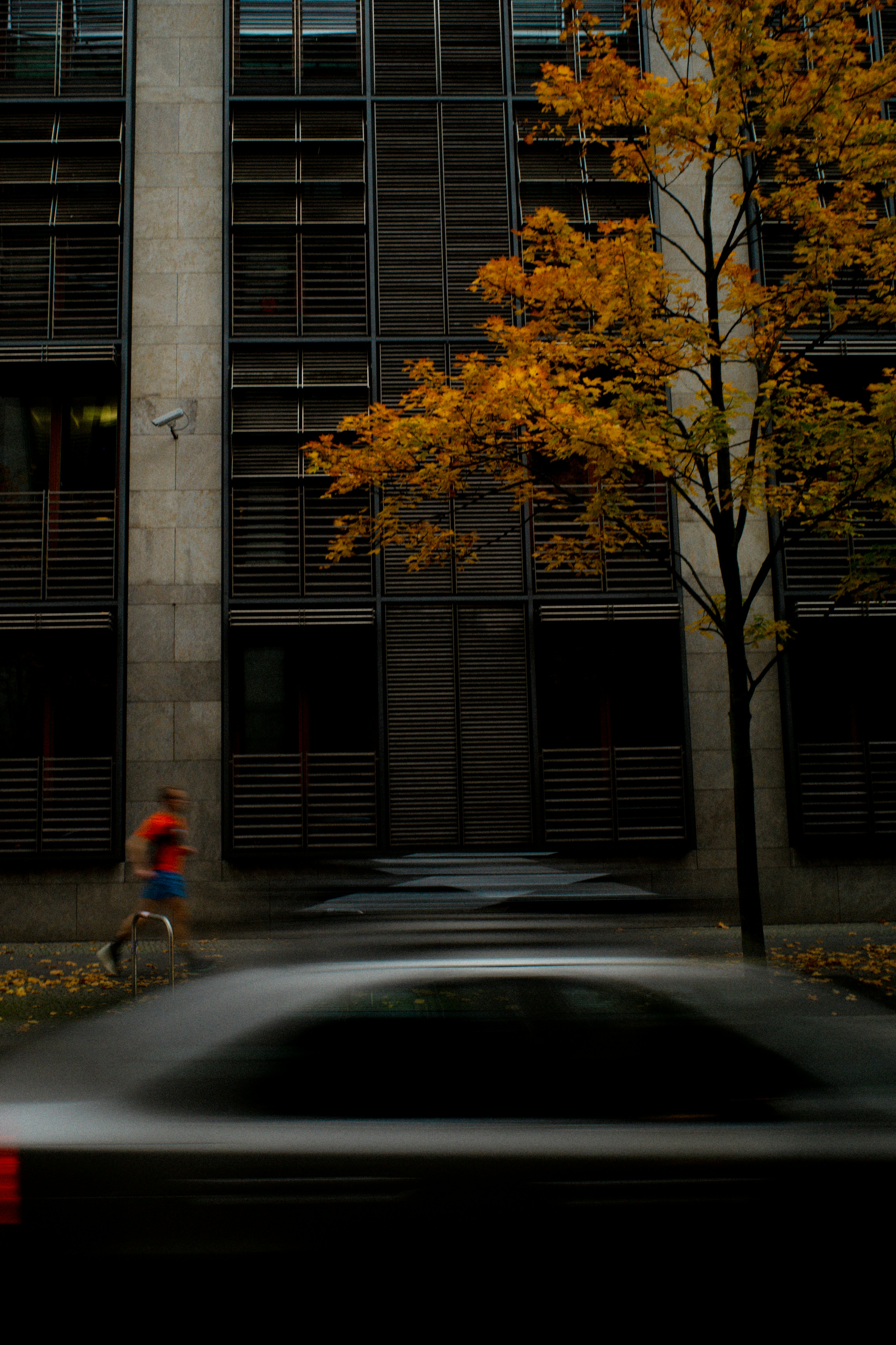 Man running past building with autumn tree