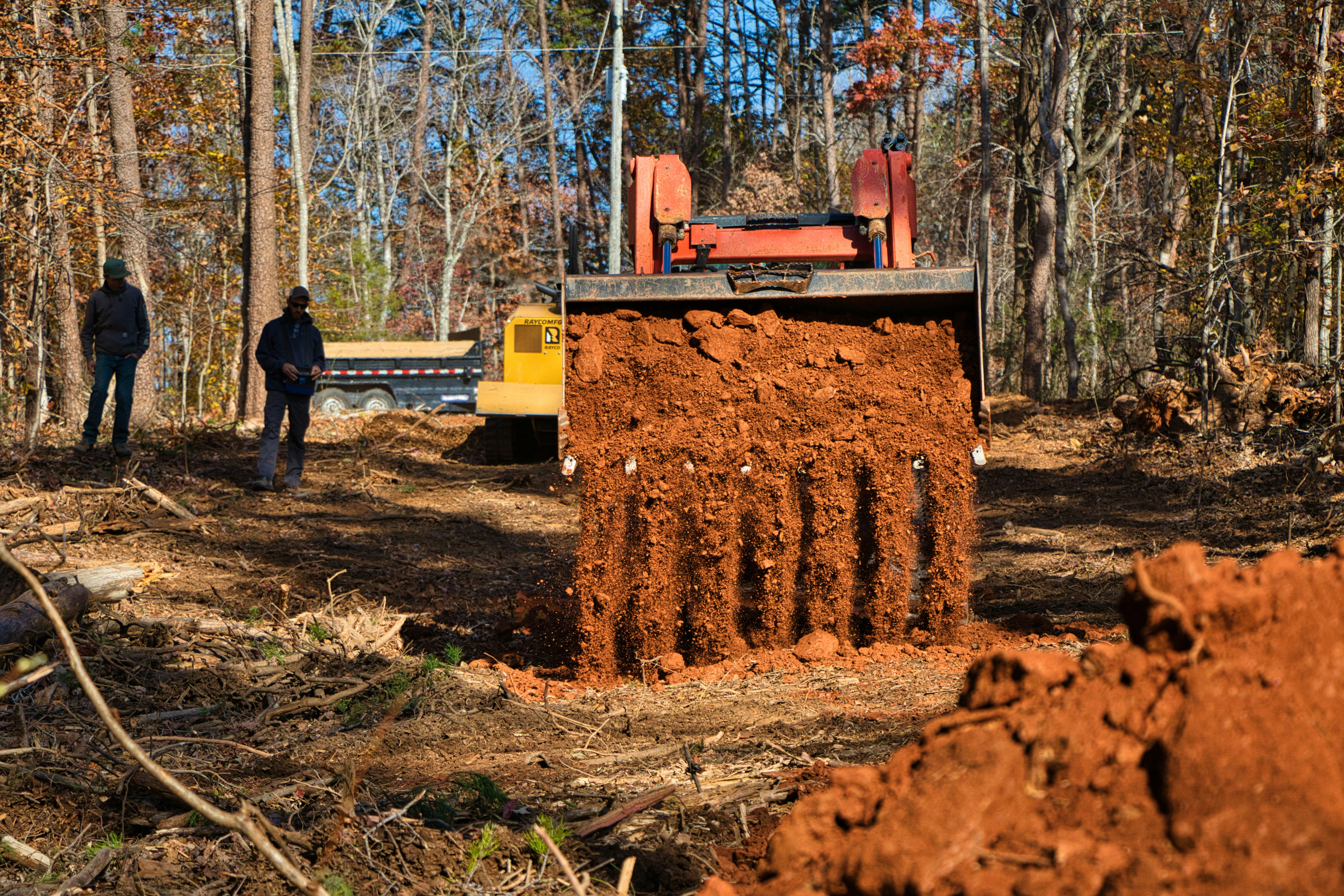 Excavator digging dirt with two people watching