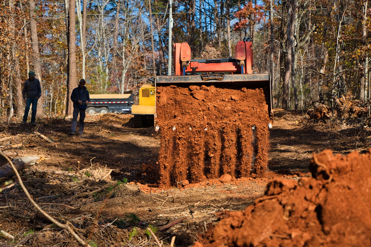 Construction excavator preparing a residential house site with septic system components nearby in a rural field.