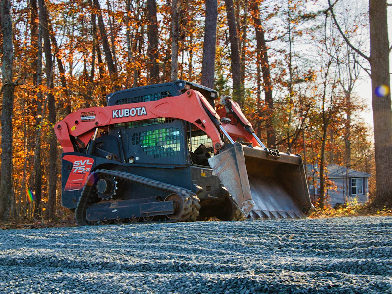 Compact track loader grading gravel on a wooded lot